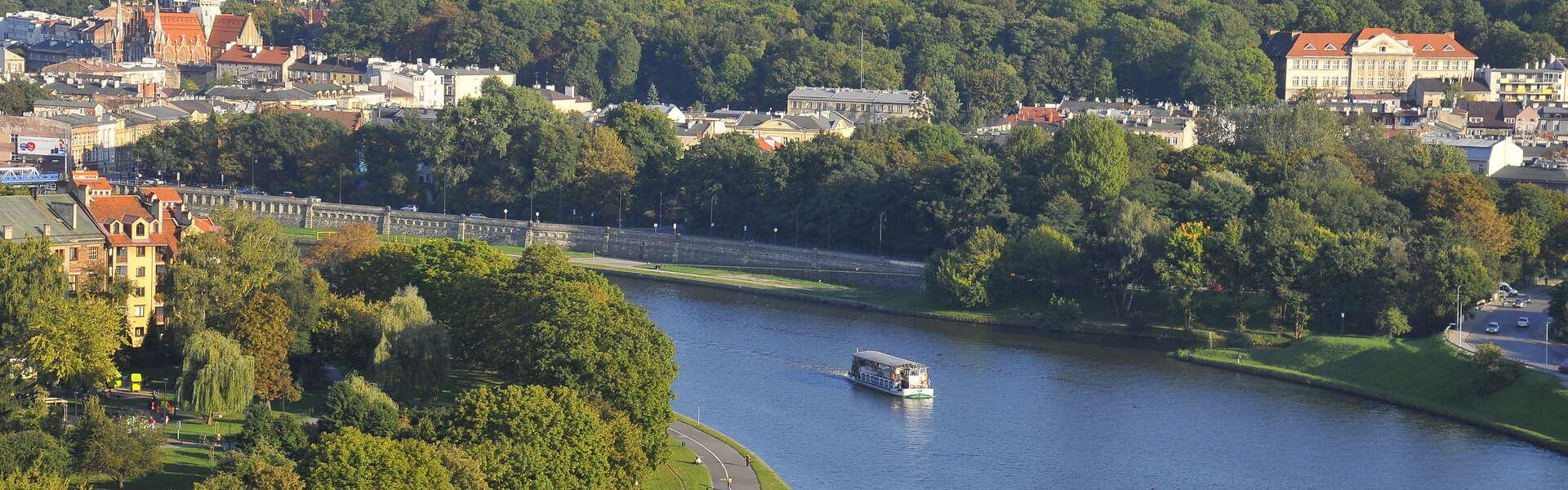 A bird’s eye view of the Vistula River, upon which a cruise ship is sailing, in the background a view of Kraków